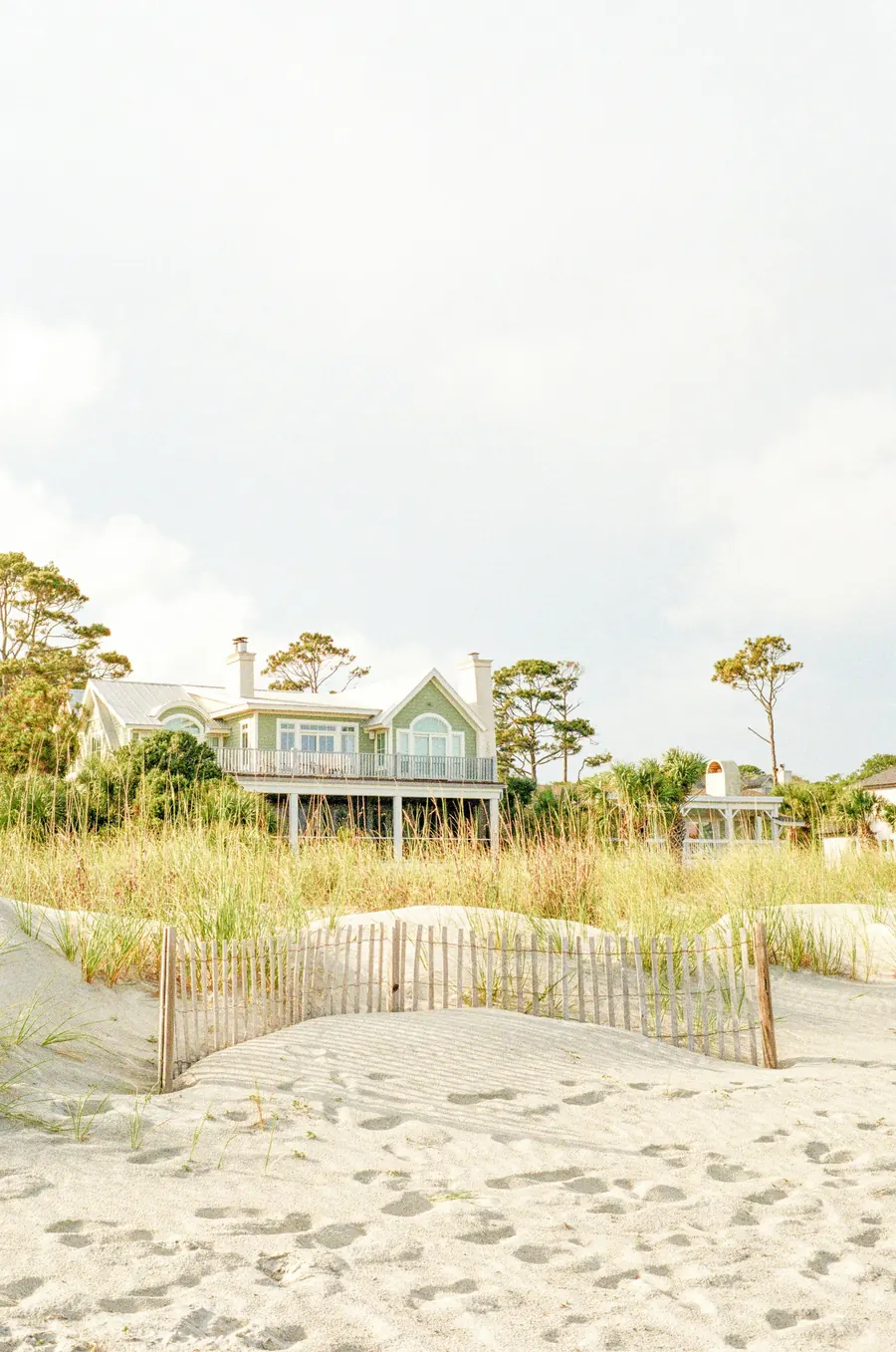 Pale wooden house on a dune behind beach grass and a low sand fence