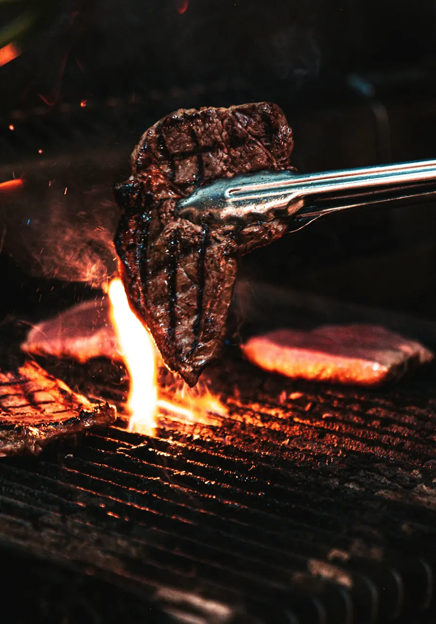 Steak lifted with tongs over open flames on a grill